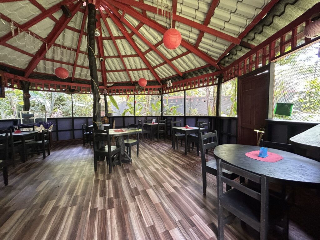 A circular open-air dining area with red beams, black furniture, and wooden flooring, decorated with red lanterns.