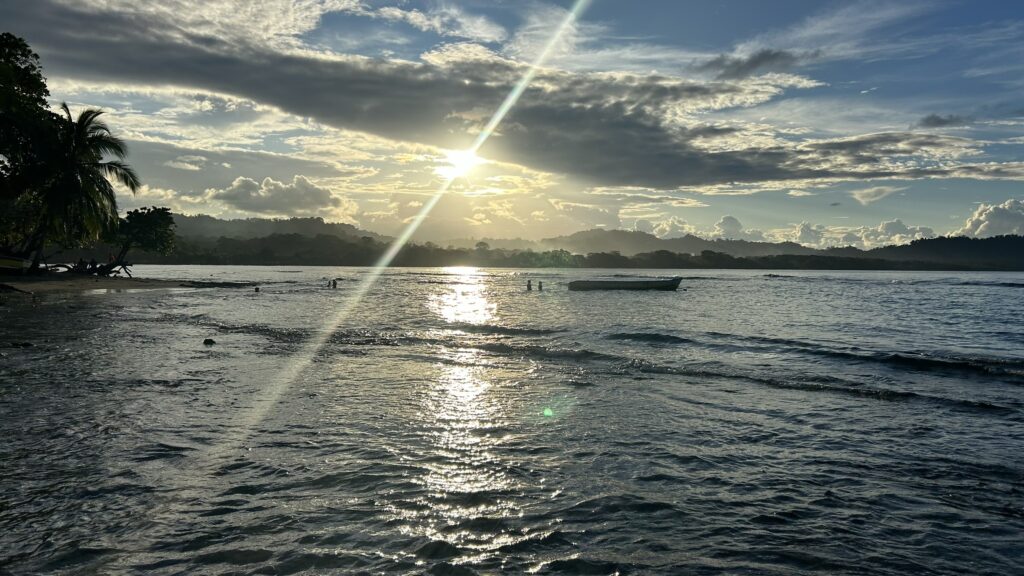 A serene view of Punta Uva Beach with calm waters, a boat, and the sun setting over the horizon.