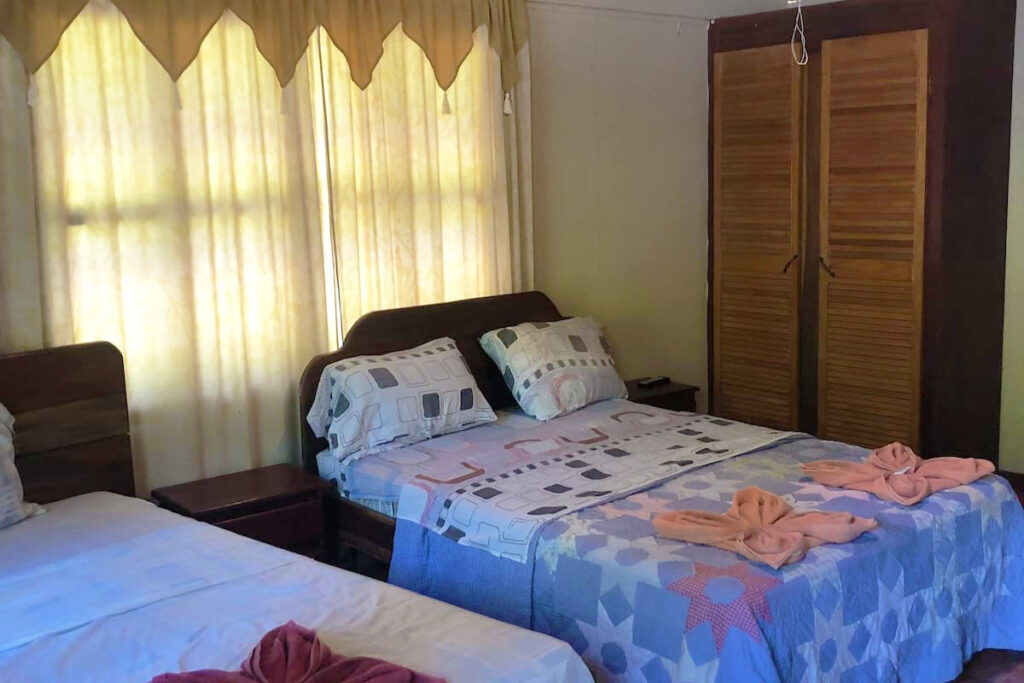 A bedroom with two beds, colorful bedding, folded towels shaped like bows, and soft yellow curtains.