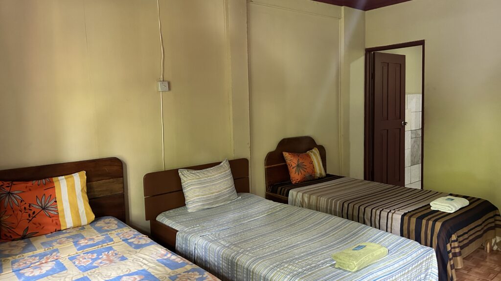 A bedroom with three single beds, each with unique bedding patterns, and a door leading to a bathroom.