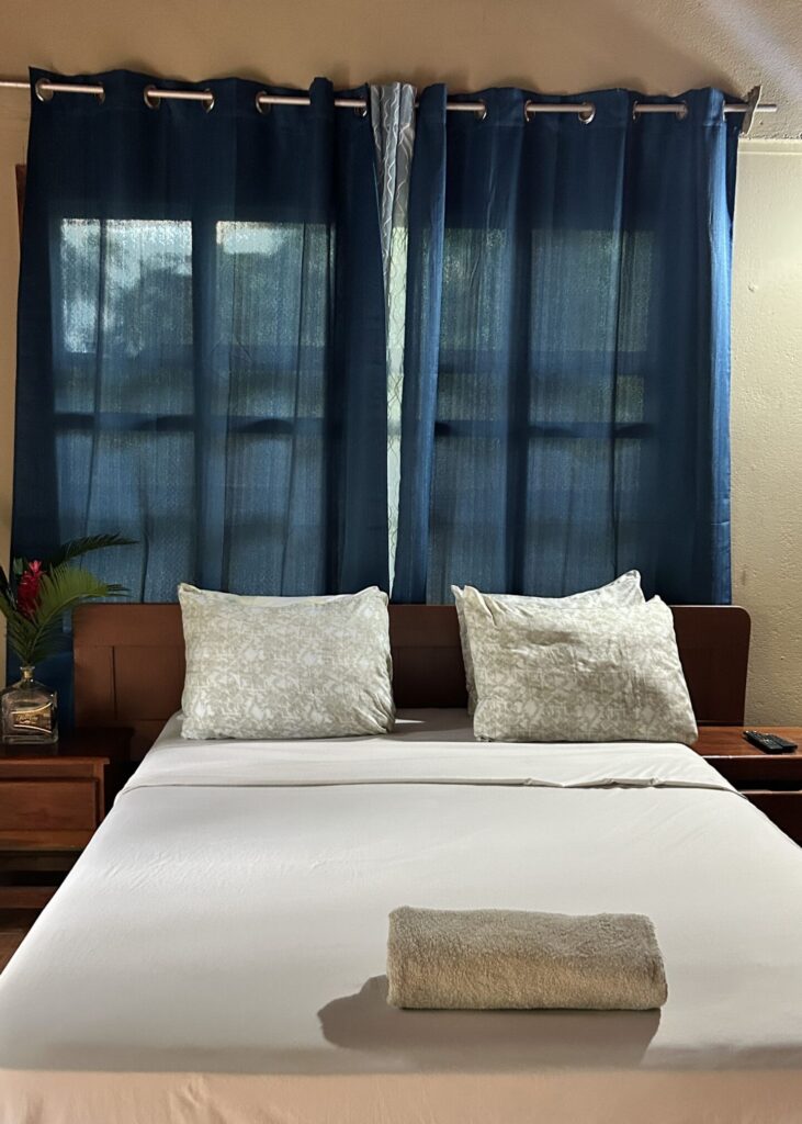 Puerto Viejo de Talamanca hotel rooms. A cozy bedroom with a neatly made bed, blue curtains, and a ceiling fan.