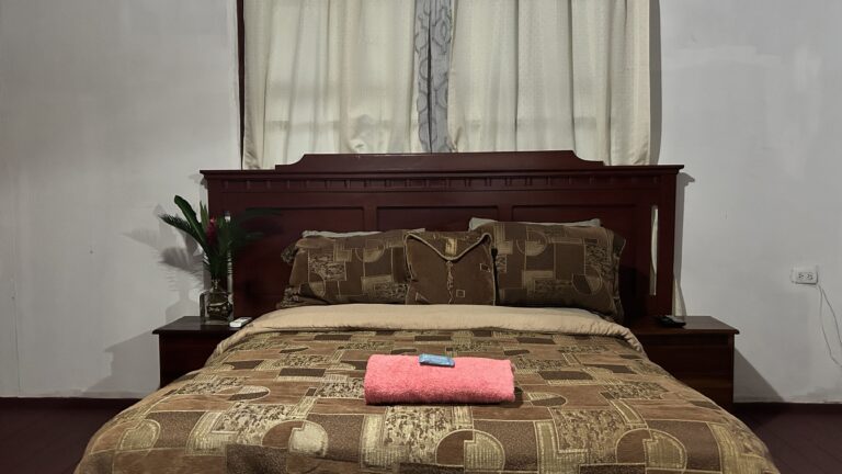 A cozy bedroom with a wooden headboard, patterned bedding, and neatly folded towels on the bed.