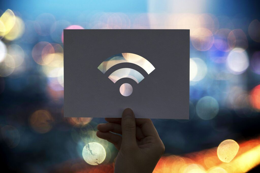 A hand holding a card with a Wi-Fi symbol cutout against a blurred background of colorful lights.